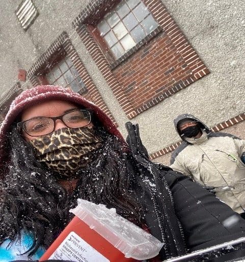 Masked individuals in snowy weather with buildings background.