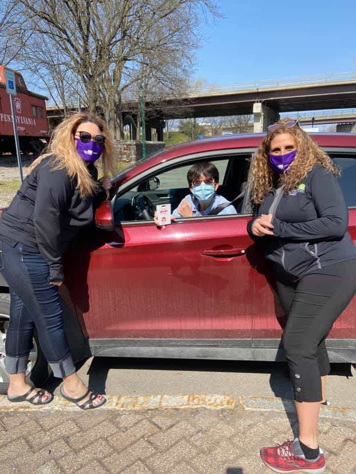 Smiling people with masks by car during daytime.