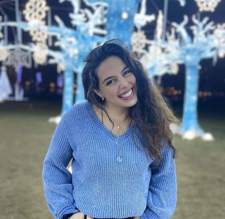 Smiling woman in blue sweater outdoors with lights.