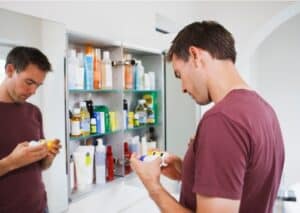 Man reading medication label near bathroom cabinet.