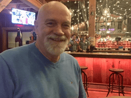 Smiling man in a rustic bar with string lights.