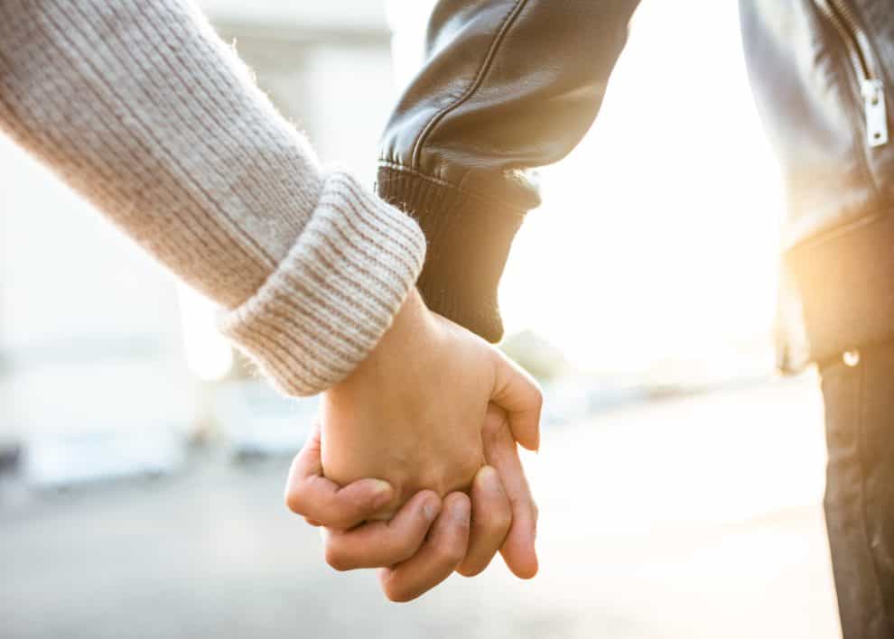 Close-up of couple holding hands in sunlight.