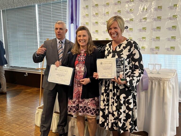 Three people holding framed certificates at event.