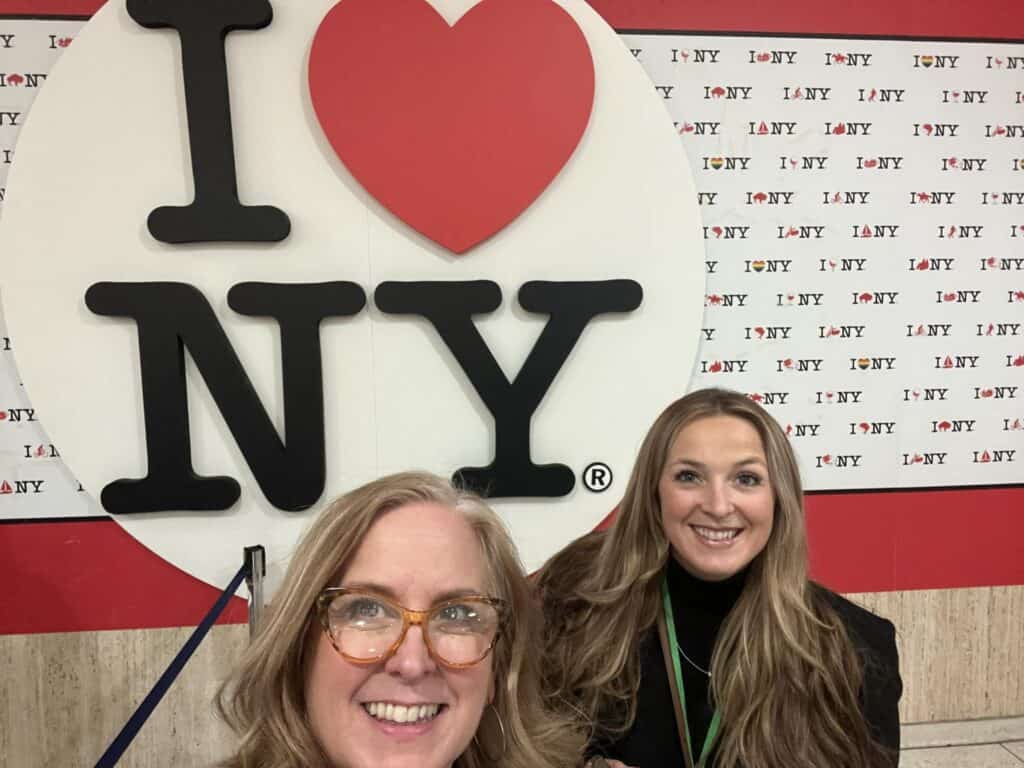 Two people smiling at 'I Love NY' sign.