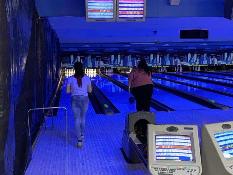 Two people bowling in dimly lit alley.