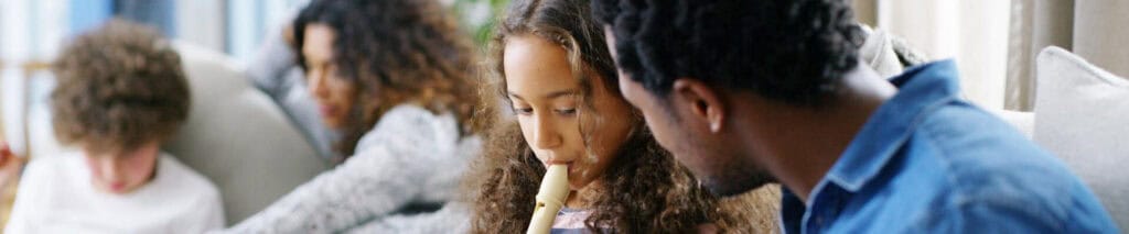 Child playing recorder with family at home.
