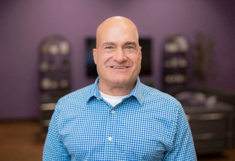 Smiling man in a blue checkered shirt indoors.