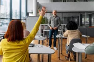 Student raising hand in classroom setting.