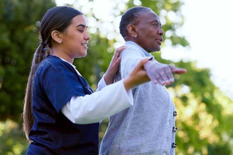 Caregiver assisting elderly woman outdoors