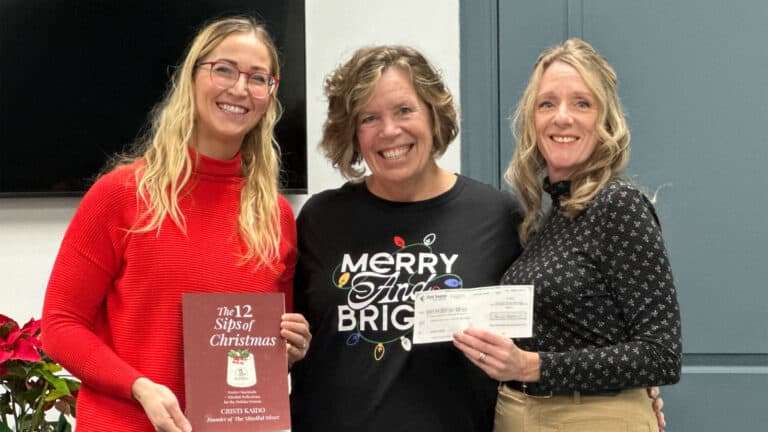Three women smiling with a book and check.