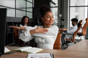 Woman stretching at office desk, smiling.