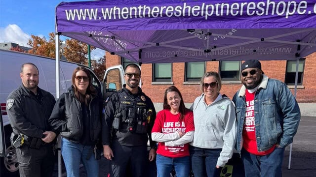 Group smiling under event tent with URL.
